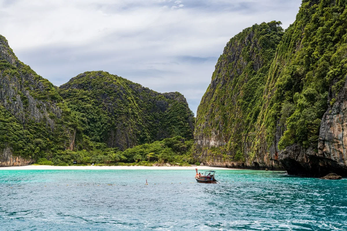 A longtail boat entering Maya Bay, a white-sand cove framed by jungle-covered limestone cliffs in the Phi Phi islands
